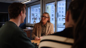 En kvinne prater med to personer på et kontor. Brukt i forbindelse med bloggpost hos Roza om å bli komfortabel foran kamera.
